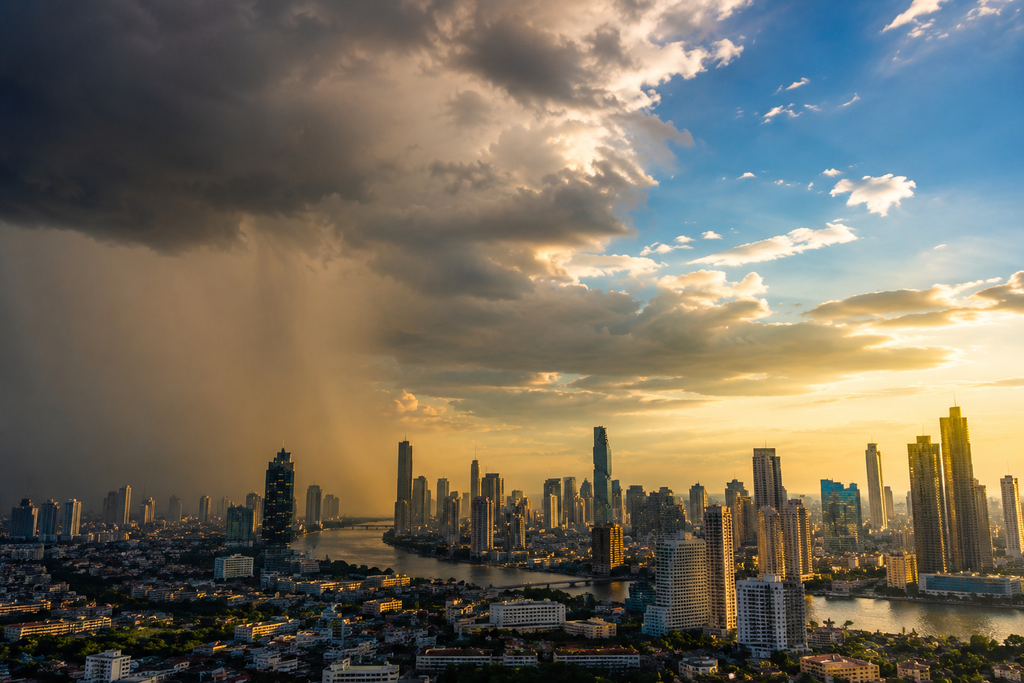 A dramatic wide shot of Bangkok skyline with half the sky covered in dark storm clouds and half showing clear blue sky with sunlight breaking through