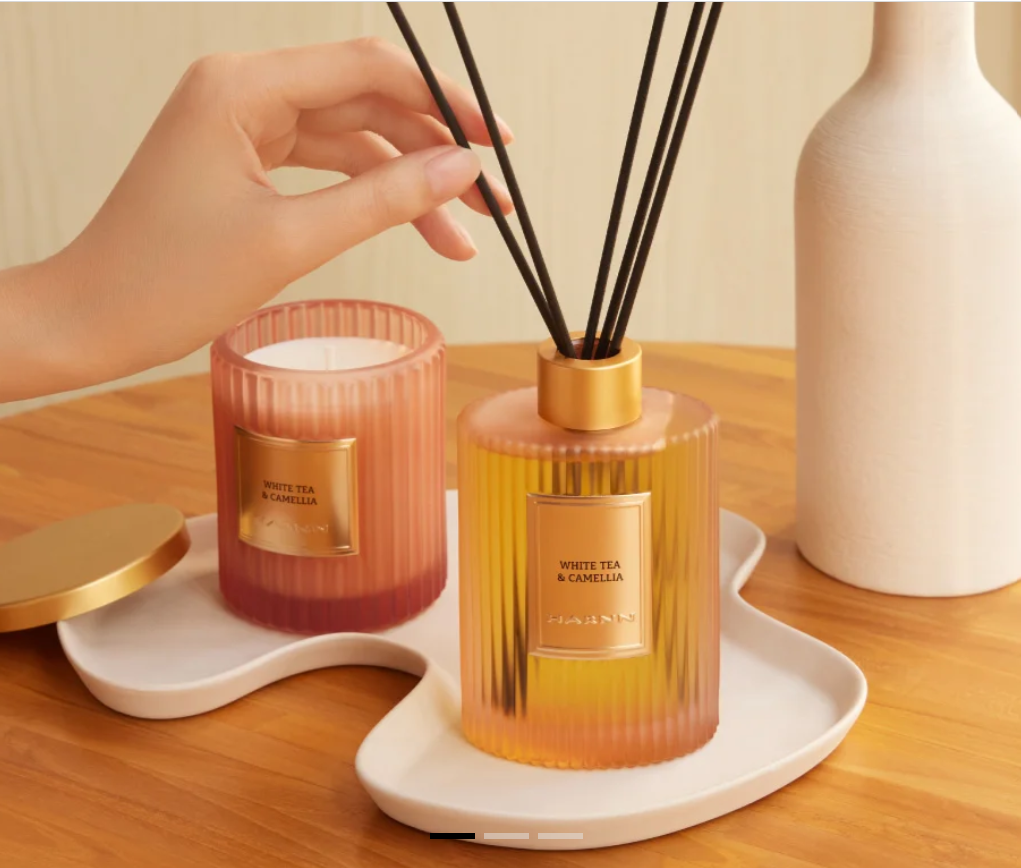 HARNN White Tea & Camellia reed diffuser and scented candle displayed on a white tray beside a ceramic vase.